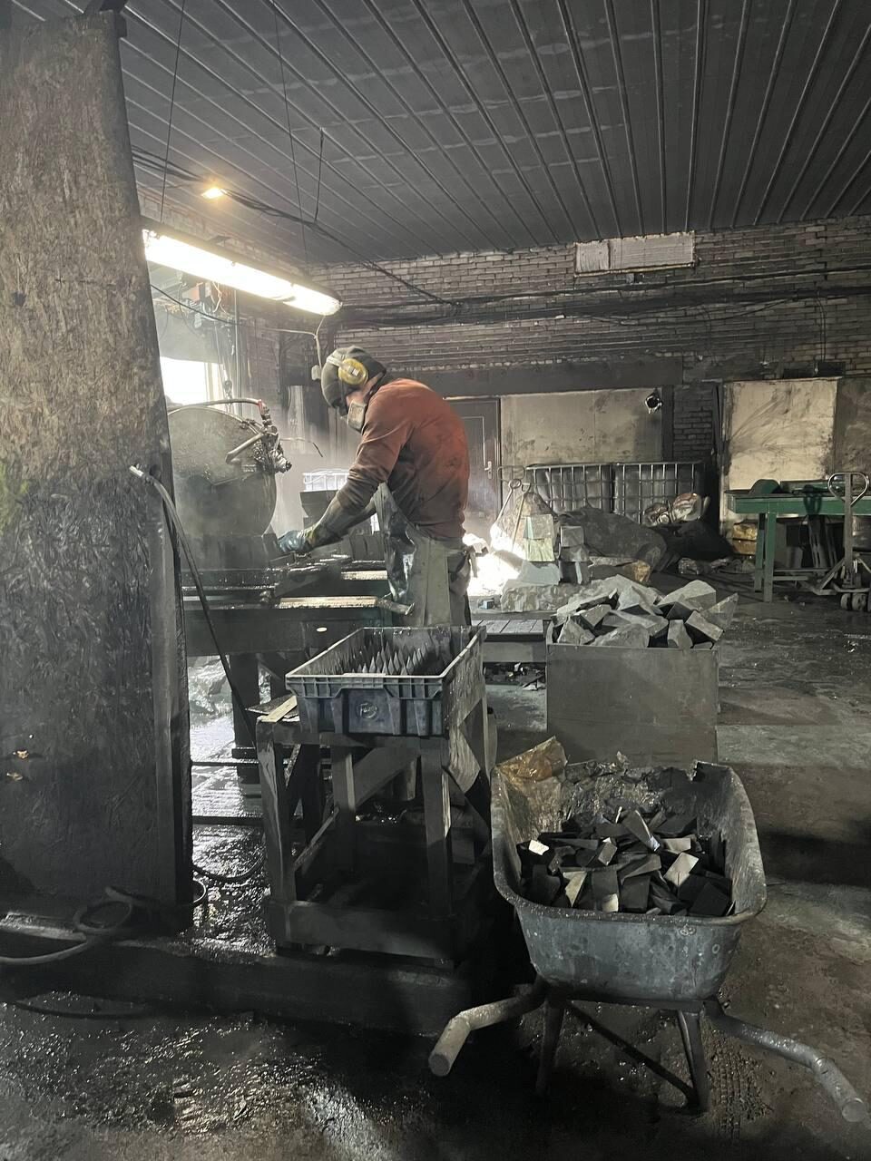 Mitarbeiter bei der Verarbeitung von dunklem Mineralmaterial in einer Werkstatt